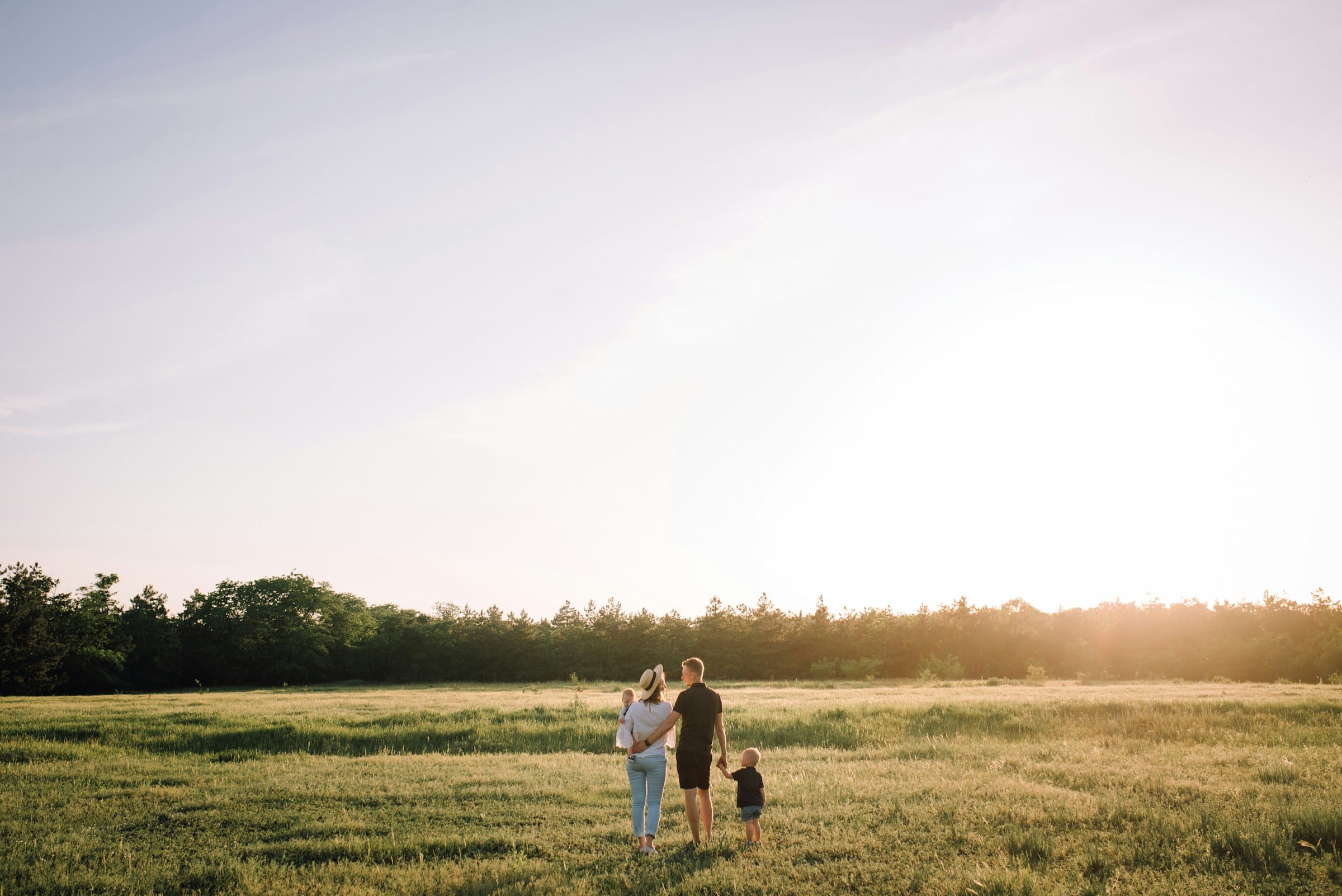 A young family walking hand in hand through a sunlit paddock at golden hour